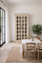 Lifestyle image of a reclaimed wood display cabinet Eknoor with glass-panelled doors and natural weathered finish. Sustainable living room furniture that can also function as a reclaimed wood wardrobe with spacious shelving.