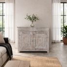 Lifestyle image of a grey-washed reclaimed wood cabinet with hand-carved floral and sunburst detailing, a vintage furniture piece perfect for rustic or bohemian interiors.