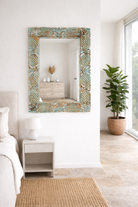 Lifestyle imagination of a carved mango wood mirror Apasmara blue in distressed turquoise finish with floral motifs. A handcrafted piece of Indian furniture ideal for vintage home decor and colorful boho interiors.