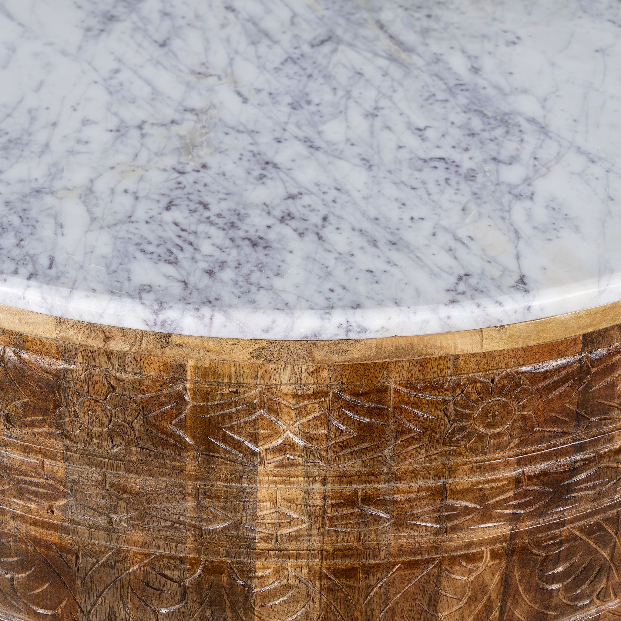 Close up image of a round hand carved mango wood coffee table with a white marble top.