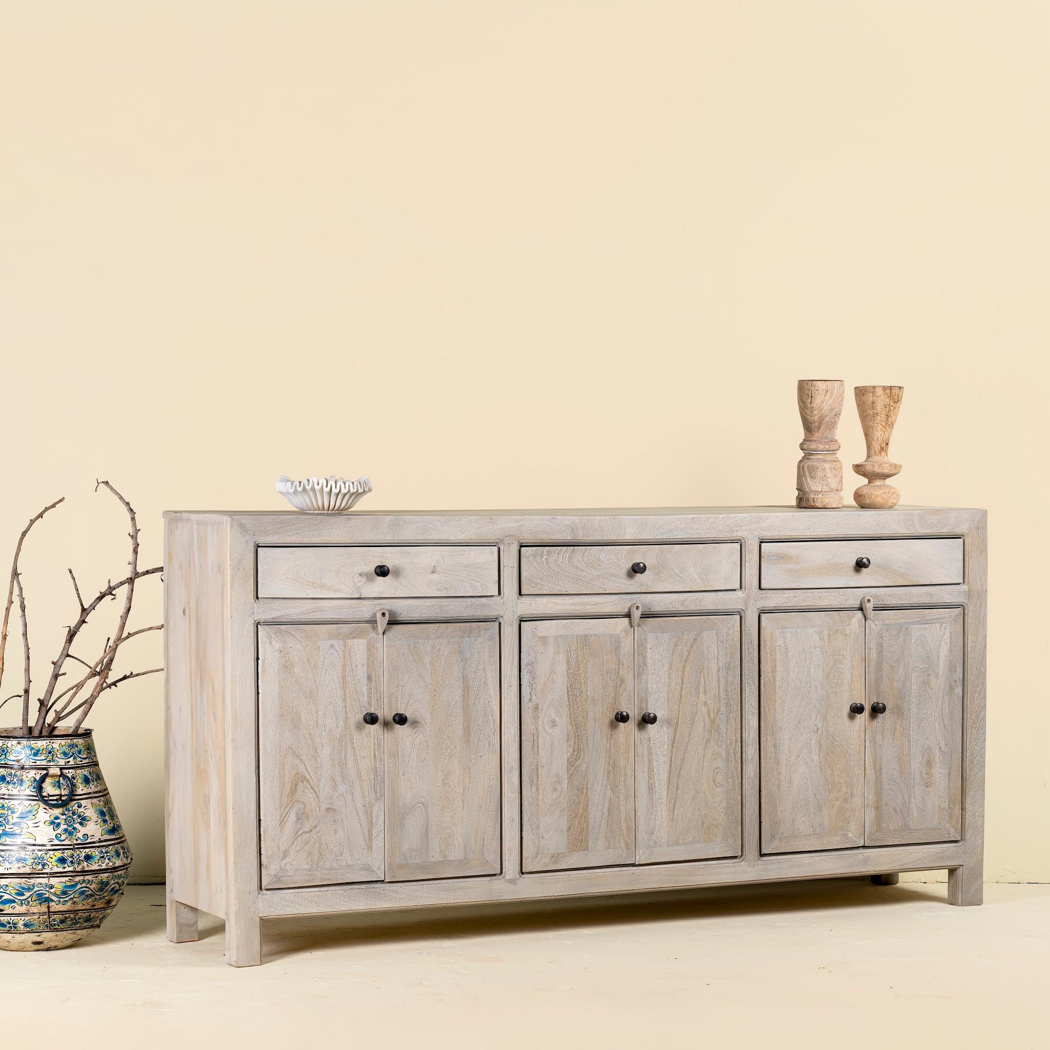 Side angle image of a sandblasted mango wood sideboard with 3 drawers and 4 cabinet doors; Mediterranean-inspired mango wood furniture, 180 × 40 × 90 cm.