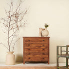 A handcrafted chest of drawers made from recycled teak wood, featuring six drawers with black metal knobs, positioned against a neutral background with decorative items on top.