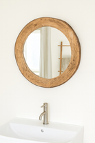 Lifestyle imagination of a round carved wooden mirror with reclaimed teak frame and rustic iron edging; Indian furniture online, 110 cm diameter, 8 cm deep.