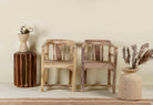 Rustic-style armchair made from reclaimed teak wood, featuring a natural, unfinished look with visible wood grain and variations in tone, and a curved backrest with vertical slats.

