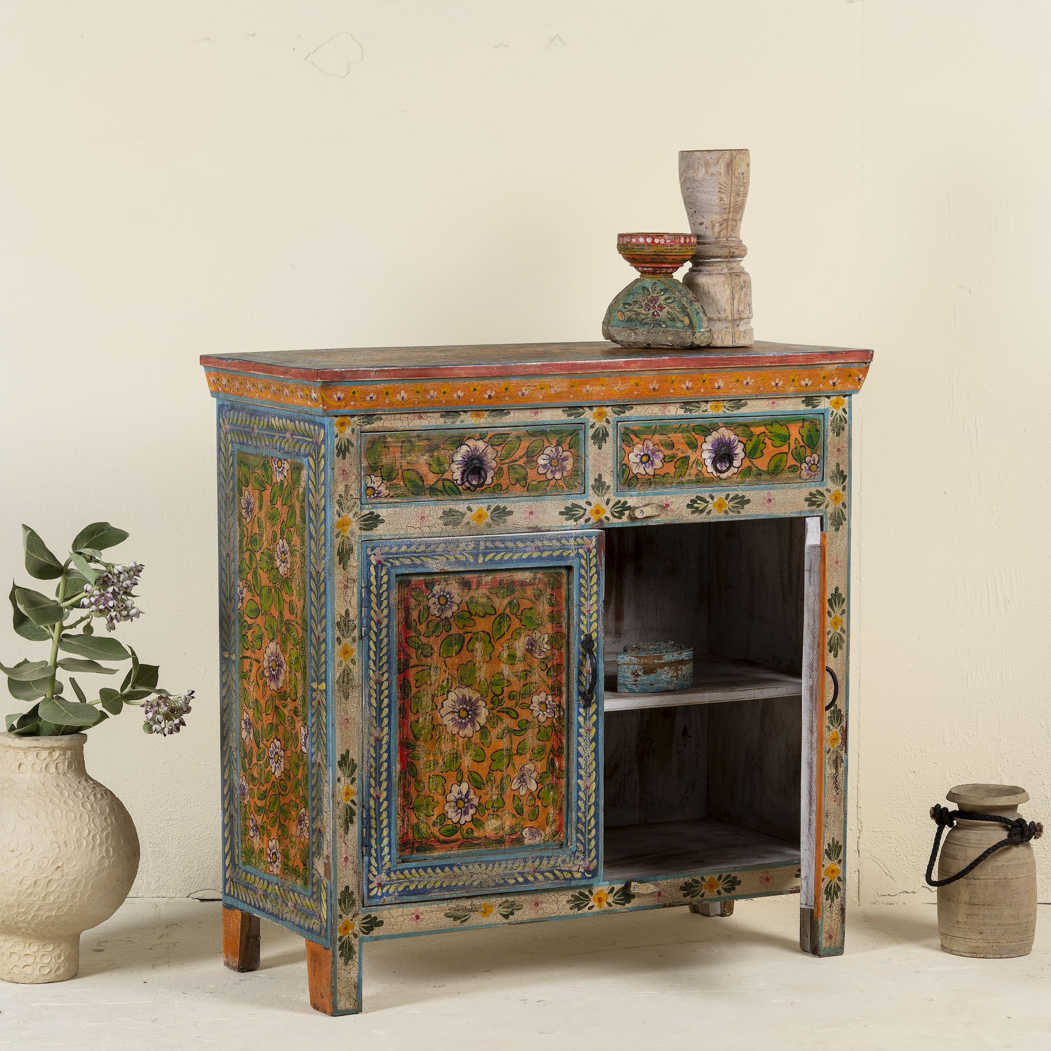 Side angle image with open door of a hand painted cabinet made of reclaimed wood with ornate floral design in vintage style.