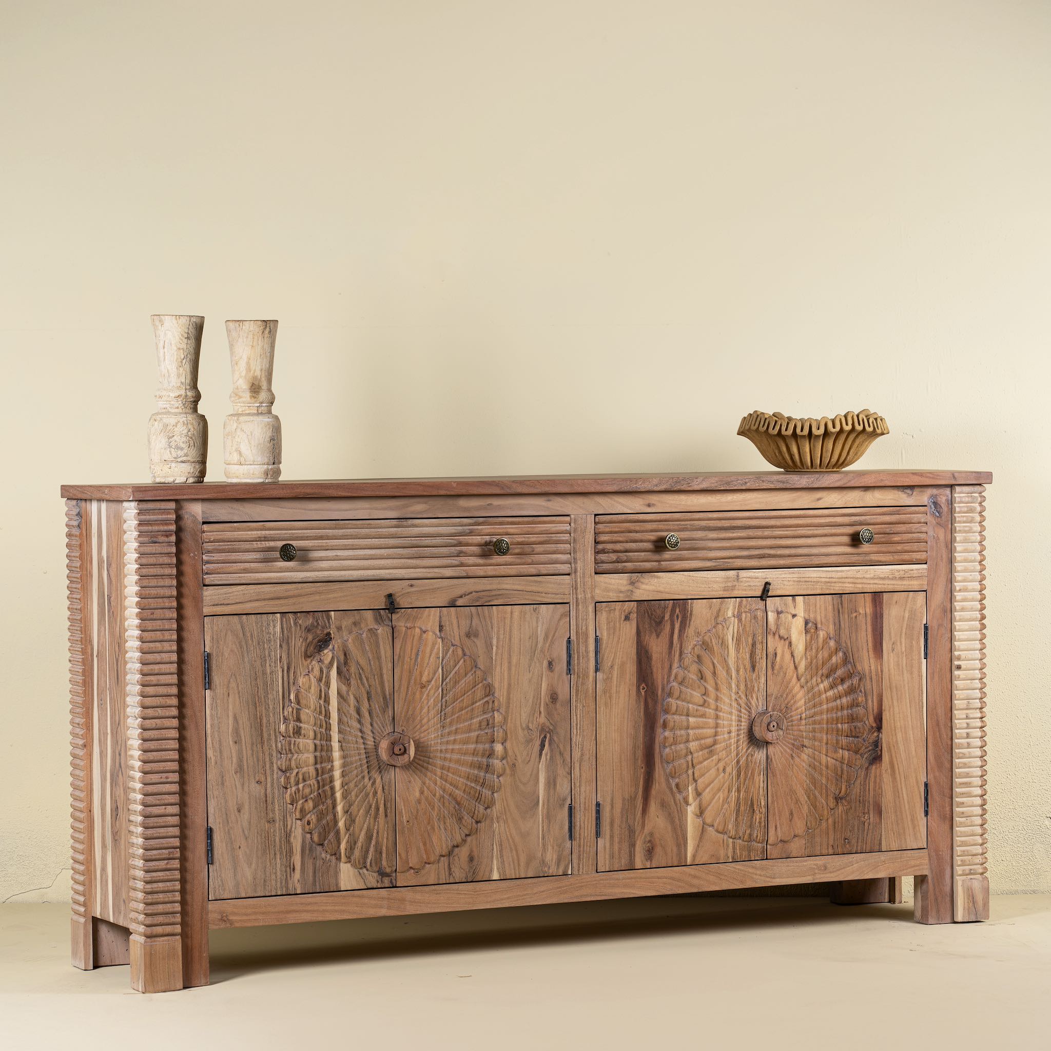 Side view of a carved acacia wood sideboard with four doors, two drawers, brass handles, and tapered legs; artisanal acacia wood furniture, 180 × 40 × 90 cm.