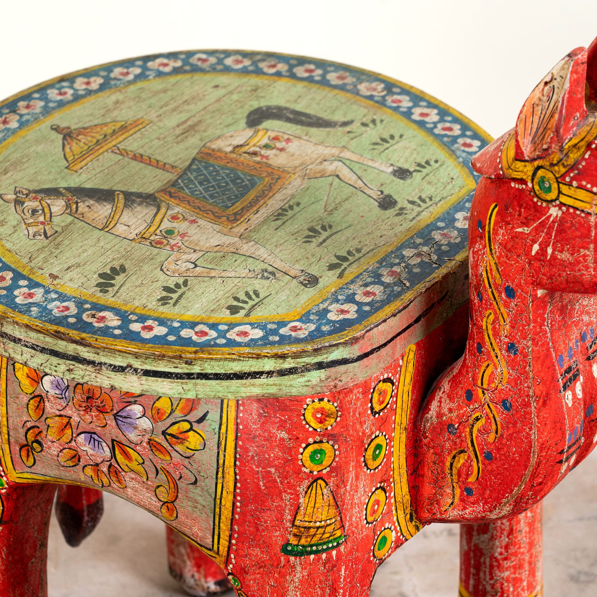 Close up image of a hand-painted wooden horse-shaped side table with floral and folk motifs, a colourful and unique vintage home accessory from India.