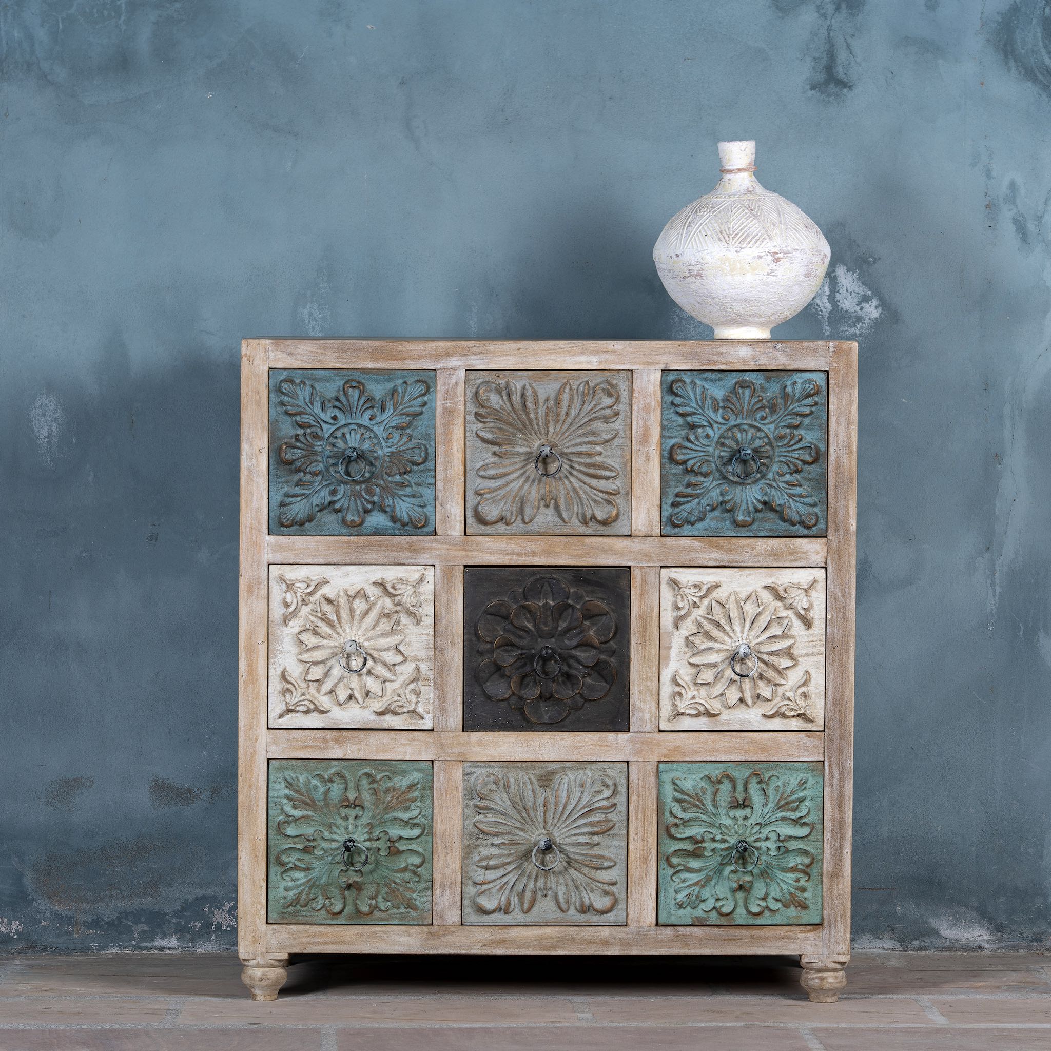 Mango wood chest of drawers Hansika with nine hand-carved floral drawer fronts in soft bohemian colours. A unique carved sideboard combining artisan design with versatile storage.