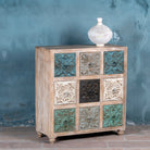 Side angle image of a mango wood chest of drawers Hansika with nine hand-carved floral drawer fronts in soft bohemian colours. A unique carved sideboard combining artisan design with versatile storage.