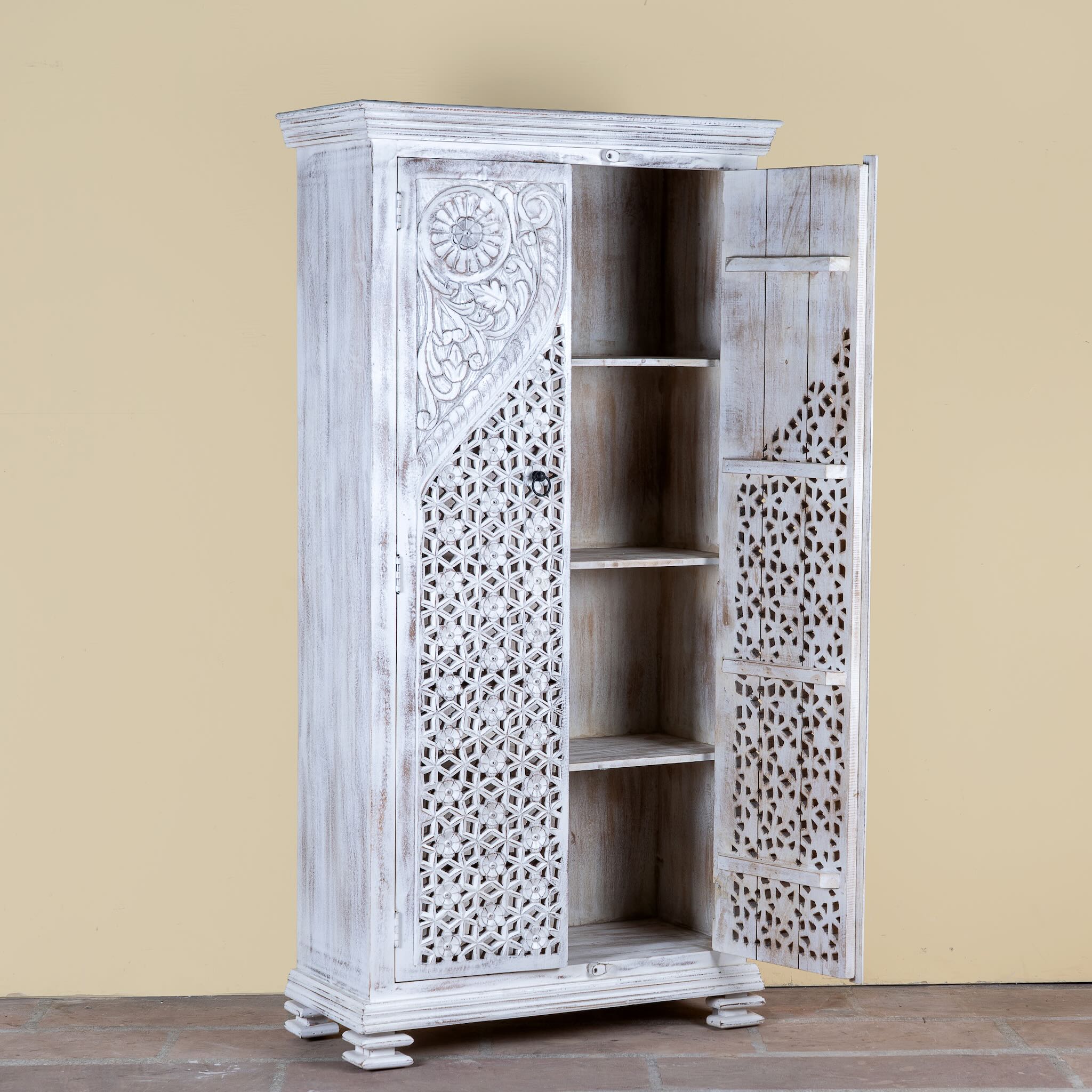 Side angle image with open door of a white-washed hand-carved wooden wardrobe made of solid mango wood, vintage furniture with Mediterranean Ibiza style, 180 × 90 × 40 cm.