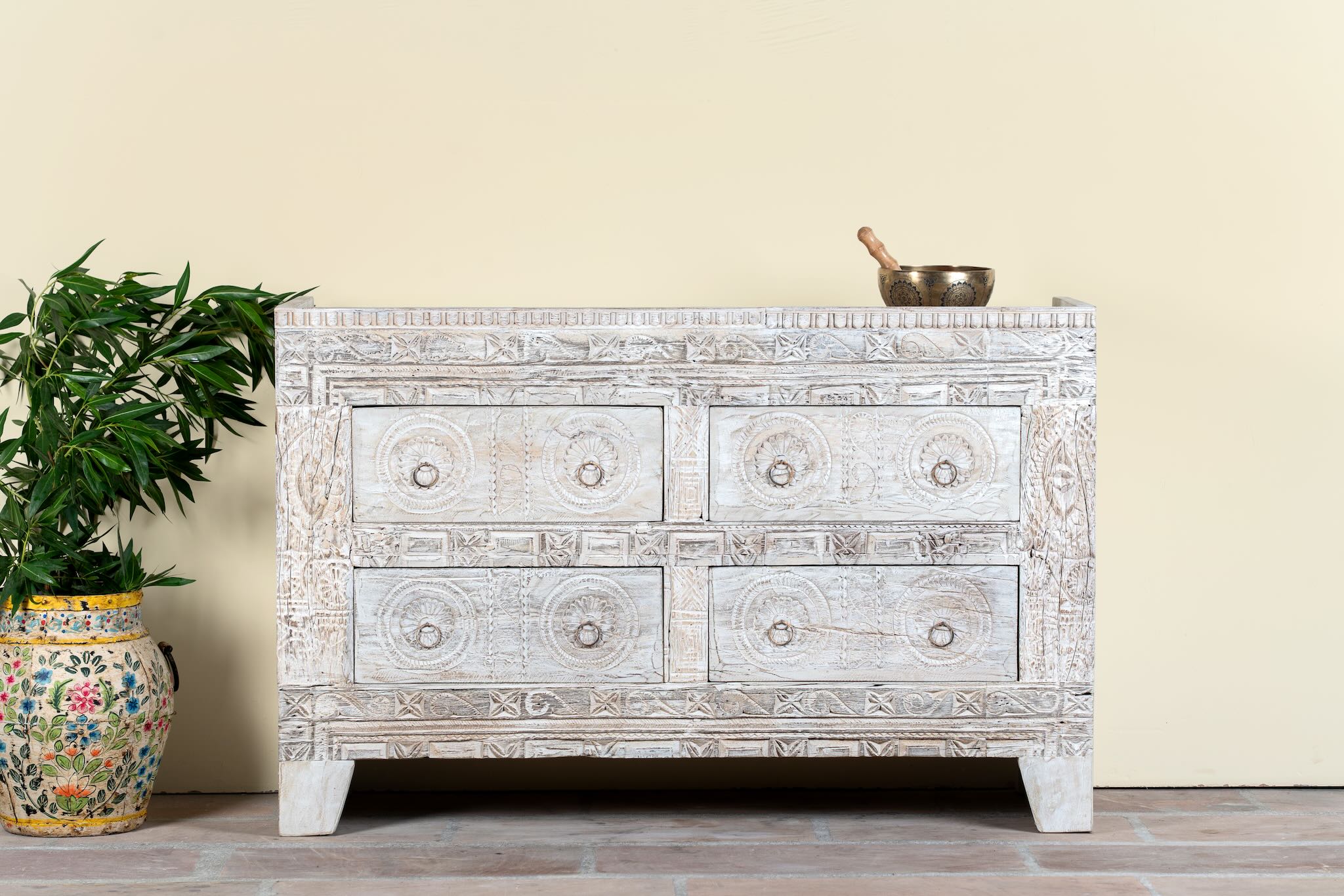 Lifestyle image of a handcrafted chest of drawers Hemali made from reclaimed wood, featuring four carved drawers with circular motifs and a whitewashed finish. A rustic, sustainable furniture piece with soft texture and elegant detailing.