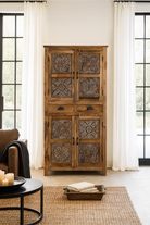 Lifestyle image of a hand-carved mango wood cabinet with floral motifs and silver finish – bedroom furniture with rustic charm and artisanal detail.