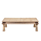 White background image of a rustic coffee table made from old reclaimed teak wood, featuring a weathered finish, turned legs, decorative carved apron, and visible metal rivets, styled with earthy decor in a minimal interior setting.
