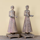 Side angle image of an antique Indian wooden temple guardian figure with weathered patina, styled beside a black-framed door in a modern living room.