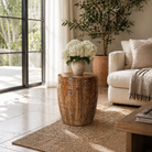 Lifestyle image of a hand-carved mango wood coffee table with barrel shape and warm rustic finish; vintage style coffee table, 45 cm diameter, 55 cm height.