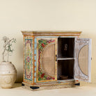 View with open doors of a hand-painted, hand-carved cupboard made of mango wood with floral design and rattan inserts.