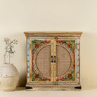 Front view of a hand-painted, hand-carved cupboard made of mango wood with floral design and rattan inserts.