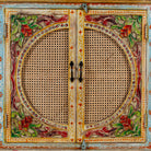 Detail view of a hand-painted, hand-carved cupboard made of mango wood with floral design and rattan inserts.