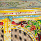 Close up image of a hand-painted, hand-carved cupboard made of mango wood with floral design and rattan inserts.