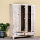 Side angle image with open doors of a hand carved creme colour mango wood wardrobe wit 2 drawers and 4 shelfs and ample storage.