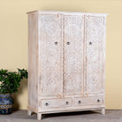 Side angle image of a hand carved creme colour mango wood wardrobe wit 2 drawers and 4 shelfs and ample storage.