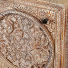 Close up picture of a pair of hand-carved bedside tables made of mango wood, featuring intricate round floral motifs on the doors, crackled vintage finish, and elegant curved legs in a distressed antique design.
