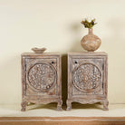 A pair of handcrafted bedside tables made from natural mango wood with intricate hand-carved floral motifs and a rustic antique finish.