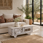 Lifestyle image of a Janash whitewashed mango wood coffee table chest with decorative iron fittings and wooden wheels 116cm