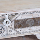 Close up image of a Janash whitewashed mango wood coffee table chest with decorative iron fittings and wooden wheels 116cm