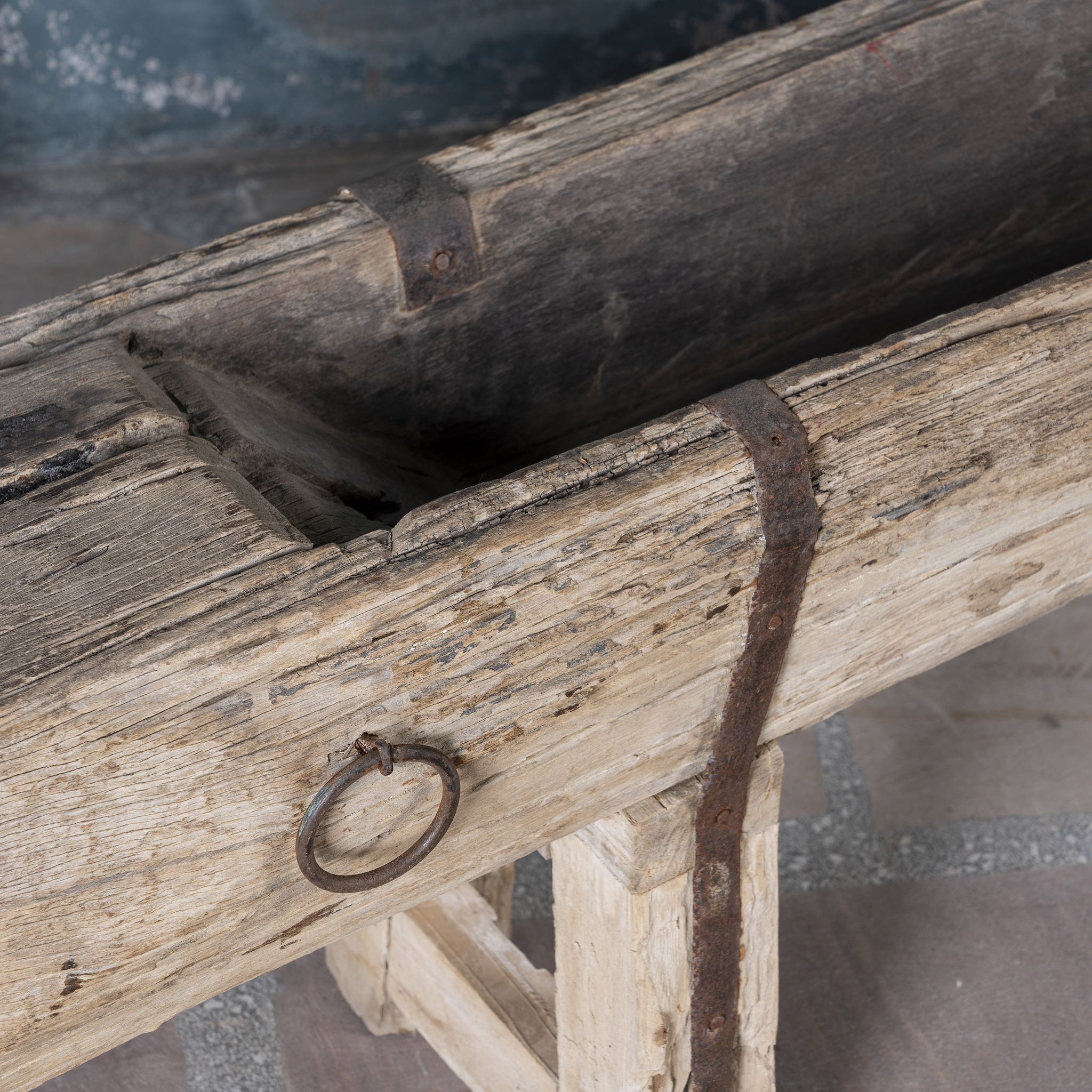 Close up picture of an antique console table repurposed from reclaimed teak wood feeding trough with carved details and iron fittings; unique furniture ideal for rustic interiors, compatible with teak wood benches, 234 × 31 × 61 cm.