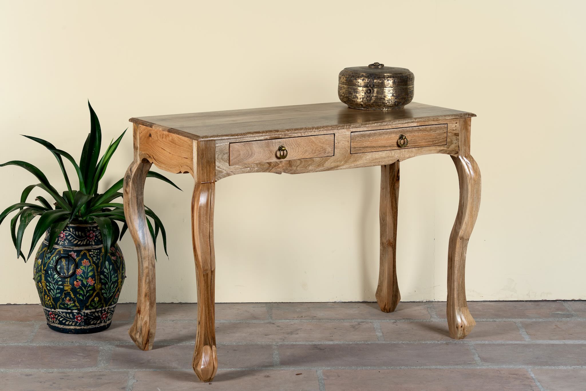 Side angle image of a desk made of natural mango wood with 2 drawers and carved legs.