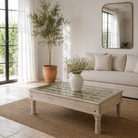 Lifestyle image of a Jayson reclaimed teak wood coffee table with glass top, removable legs, and hand carved antique Indian ceiling panel.