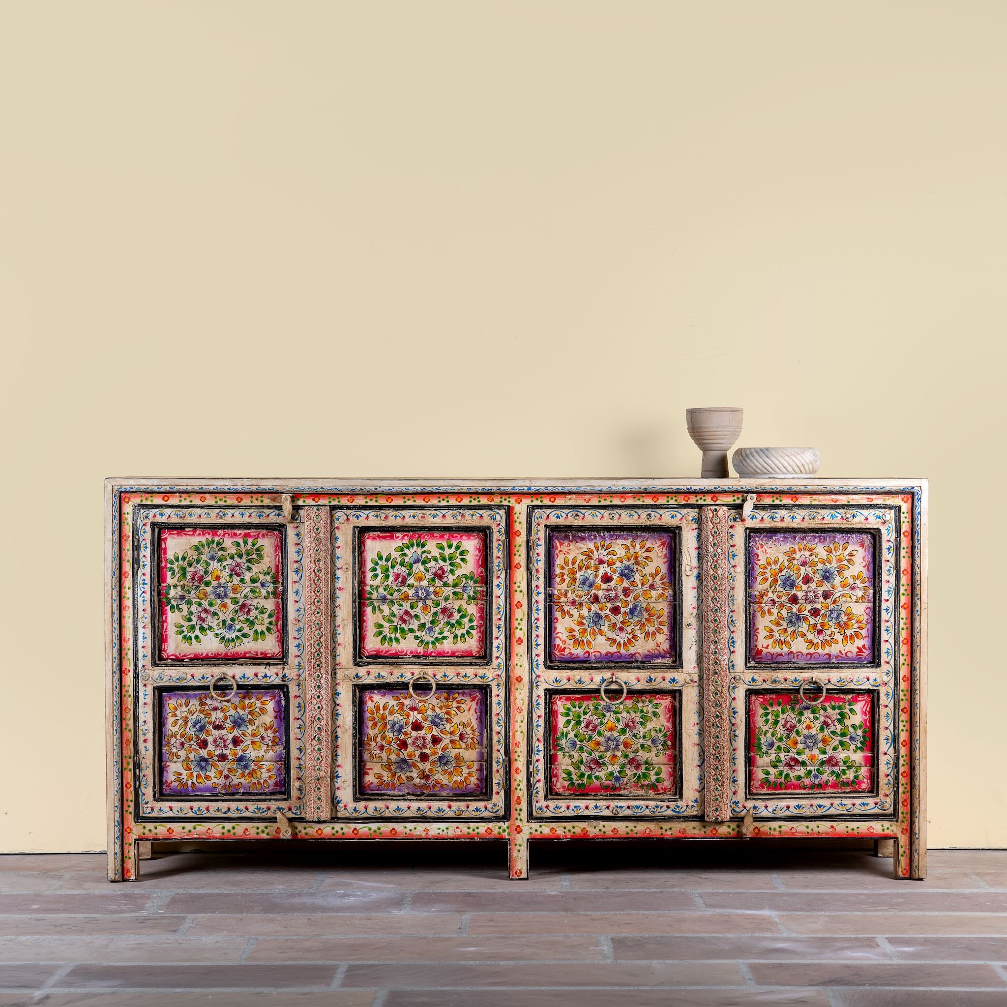 Decorative wooden sideboard with colorful floral patterns on a beige wall background