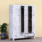 Sde angle image with open doors of a white washed hand carved wardrobe made of mango wood in floral design with 2 drawers and ample inside storage.