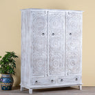 Side angle image of a white washed hand carved wardrobe made of mango wood in floral design with 2 drawers and ample inside storage.