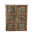 White background image of a antique wall panel made from an old teak wood window frame, featuring hand-painted blue floral motifs on a distressed natural wood background, with ornate yellow, white, and blue border accents and decorative metal ring pulls.
