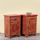 Side angle image of a Joven pair of hand painted reclaimed wood nightstands with one drawer, one cabinet door, floral artwork, and vibrant red boho style finish.