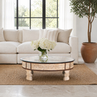 Lifestyle image of a round reclaimed wood coffee table with glass top and hand-carved Indian design; hollow interior, 70 cm diameter, 30 cm height.