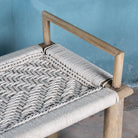 Close up of a Japandi style wooden bench with hand woven seating in a mediterrane scene.