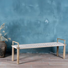 Side view of a Japandi style wooden bench with hand woven seating in a mediterrane scene.