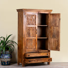 Side angle image with open door of a dark brown mango wood cabinet with hand carvings, 2 drawers and ample storage.