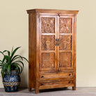 Side angle image of a dark brown mango wood cabinet with hand carvings, 2 drawers and ample storage.