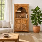 Lifestyle image of a hand-carved mango wood shelf with floral detailing, open shelf, and carved legs – carved wooden furniture in honey finish for rustic and Mediterranean interiors.