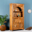 Side angle image of a hand-carved mango wood shelf with floral detailing, open shelf, and carved legs – carved wooden furniture in honey finish for rustic and Mediterranean interiors.