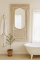 Lifestyle image of a white washed tall vintage wall mirror with hand-carved mango wood frame; rustic hand carved mirror, 86 × 160 × 5 cm.