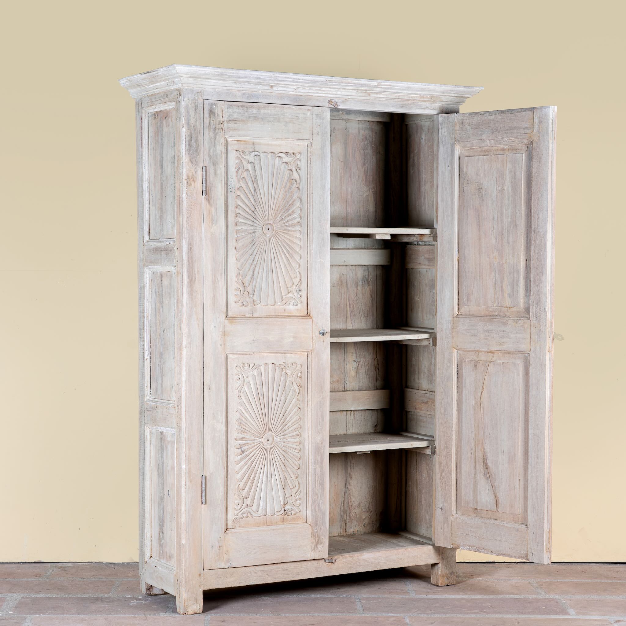 Side angle image with open doors of a Kaiden reclaimed teak wood wardrobe with hand-carved Indian details, double doors, and vintage whitewashed finish.