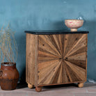 Side angle image of a reclaimed wood sideboard with sunburst carved doors, sliding black marble top, and rustic finish, ideal for rustic interior design.