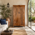 Lifestyle image of a Kalki hand carved mango wood wardrobe with botanical carved doors, removable shelves and hanging rail, 110x56x190cm