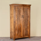 Side angle image of a Kalki hand carved mango wood wardrobe with botanical carved doors, removable shelves and hanging rail, 110x56x190cm