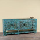 Side angle image of a Kalpana reclaimed wood console table with blue distressed finish, carved doors, three drawers, enclosed storage and open lower shelf.